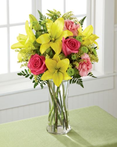 Light, lovely, and set to surprise and delight your recipient with it's bright blooms, this flower bouquet speaks to the magic that each day holds. Brilliant yellow Asiatic Lilies are surrounded by hot pink roses, pink carnations, yellow solidago, and lush greens, beautifully arranged in a classic clear glass vase to create a gift that exudes warmth and happiness. A wonderful way to celebrate a birthday, or express your thank you, or congratulations wishes!