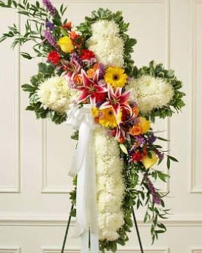 A solid white standing cross with a bright flower break, this beautiful floral tribute shows your compassion, faith and love during this difficult time. The arrangement is created from fresh white mums and bright-colored roses, lilies, Gerbera daisies, carnations and more. Traditionally sent directly to the funeral home by family members or friends and displayed on a stand.