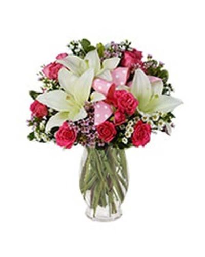 Light pink roses, pink waxflower, white Asiatic lilies and white Monte Casino blooms dance vividly around a playful pink polka dot ribbon in this glorious arrangement set in a pink fluted vase.
